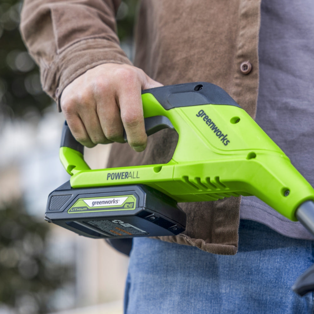 Person holding a green Greenworks power tool outdoors