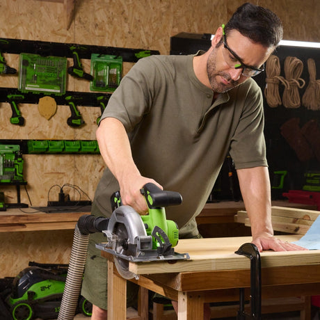 Man using a circular saw in a workshop with tools and equipment in the background.