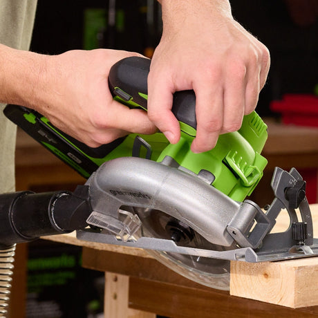 Person using a green and black circular saw on a wooden surface with a blurred workshop background.