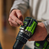 A close-up of a person holding a DeWalt cordless drill, showing the green and black trigger switch area with their fingers, set against a blurred workshop background.